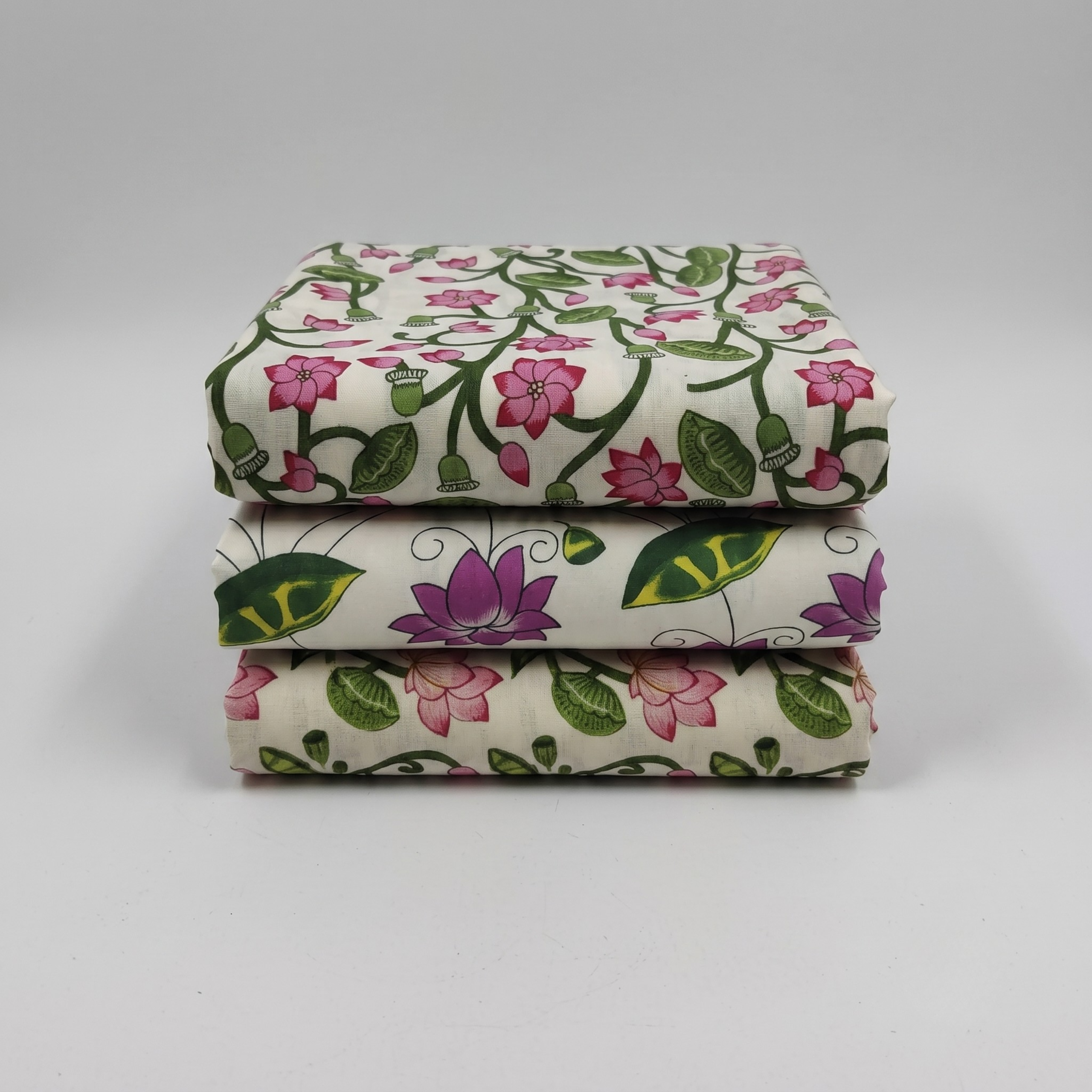 Three folded printed vastra pieces with lotus and leaf motifs, arranged as a Pushtimargiya shringar combo set.