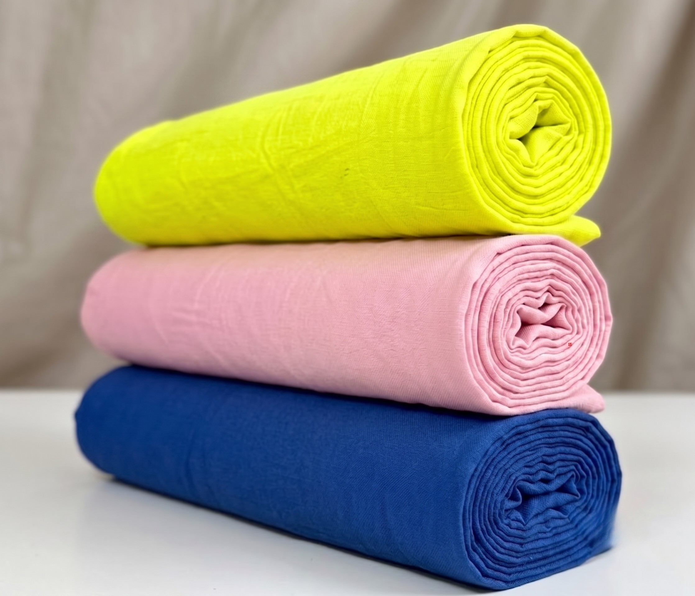 Three rolled plain fabric pieces stacked in a Pushtimargiya shringar combo for Thakorji vastra use