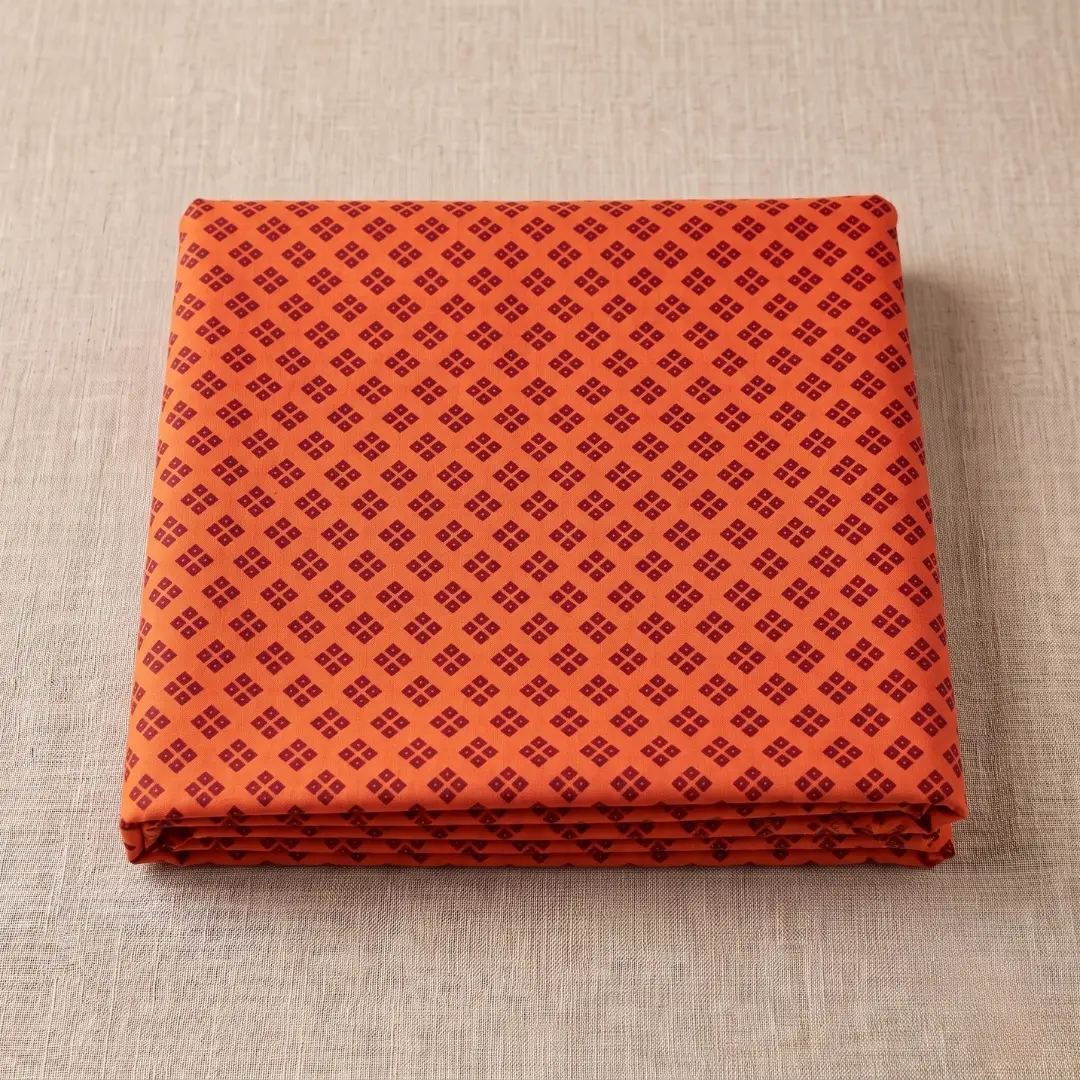 Soft orange and brown printed bandhani vastra for thakorji vastra seva neatly folded on a beige background.