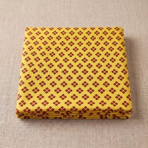 Stacked yellow bandhani vastra cloth featuring deep red geometric motifs.